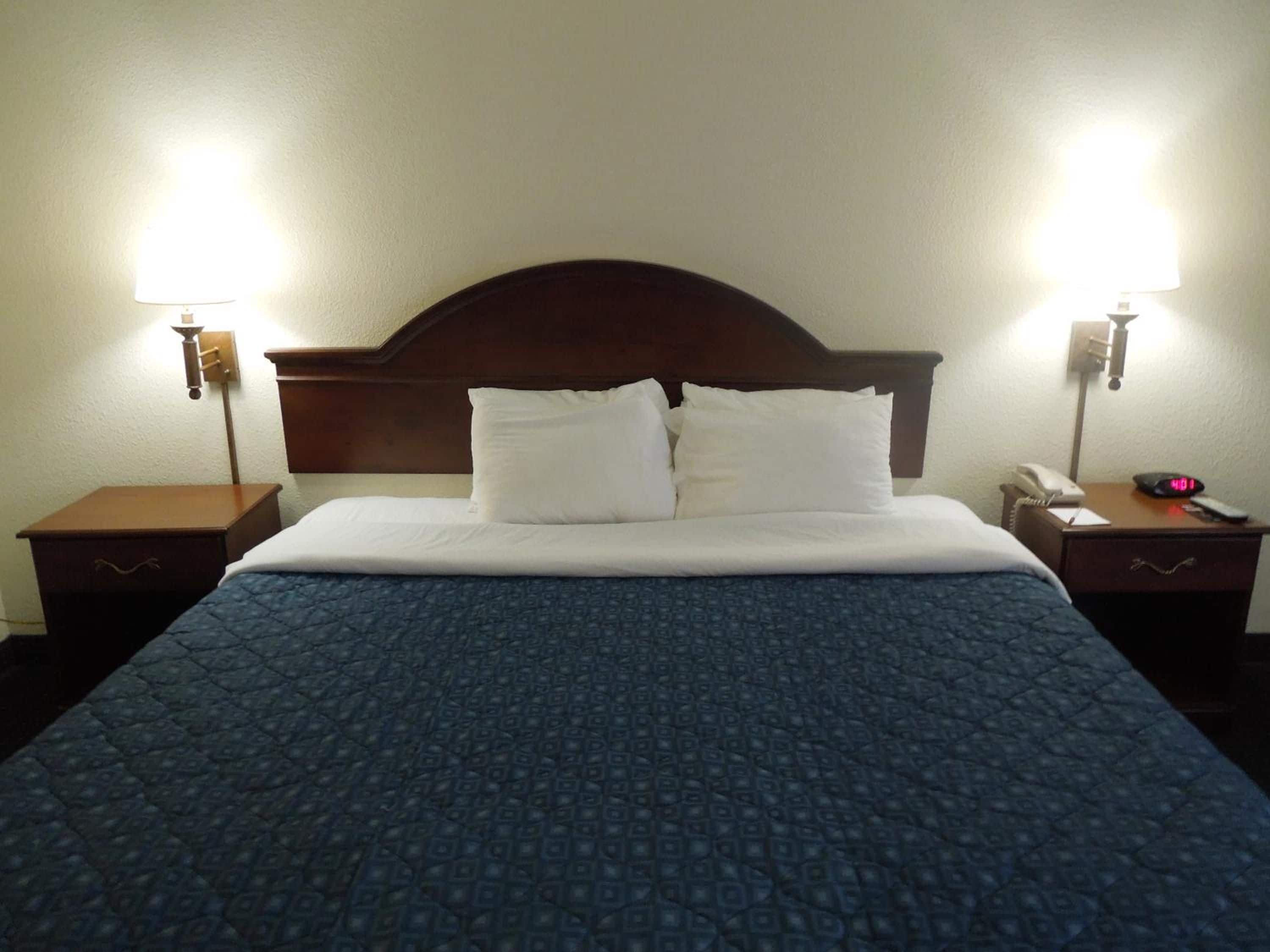Una habitación de hotel con una cama, dos mesitas de noche, una lámpara, un reloj y un teléfono.
