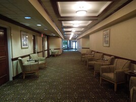 A hotel corridor with patterned carpet, chairs, and framed pictures on the walls.