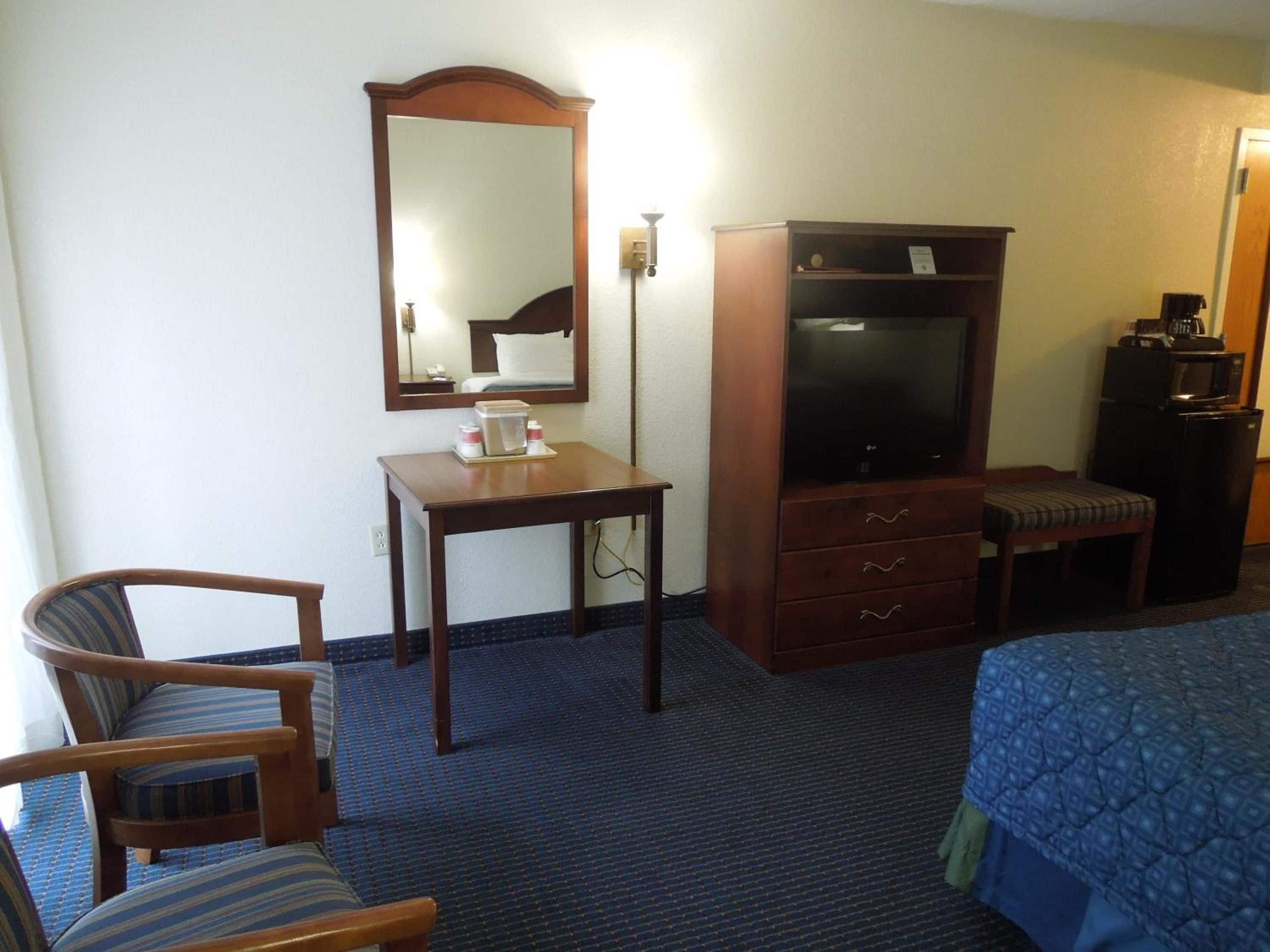 A hotel room with a bed, a desk, a chair, a television, and a minibar.