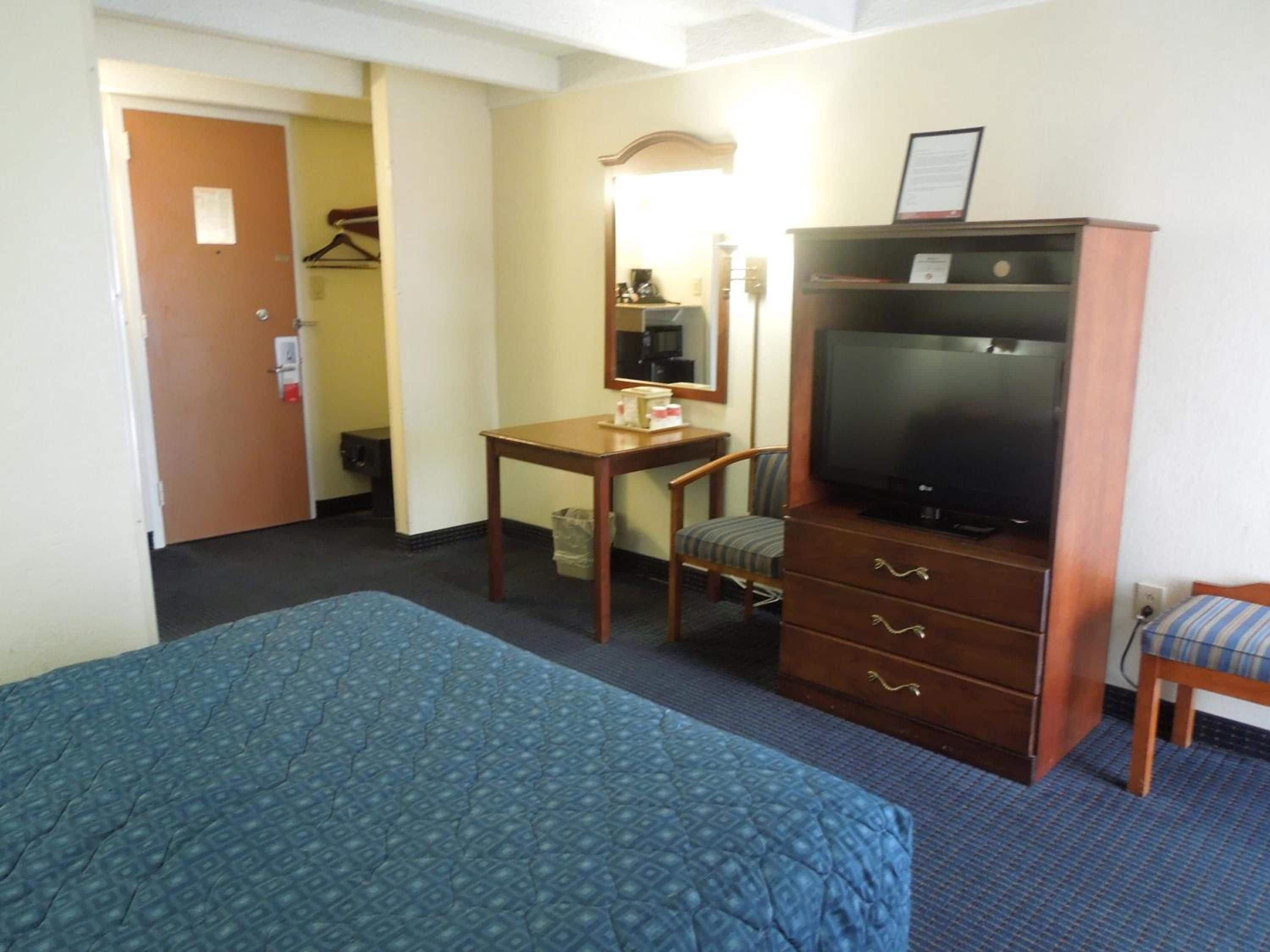 Een hotelkamer met een bed, een bureau, een televisie, een stoel en een kledingkast.