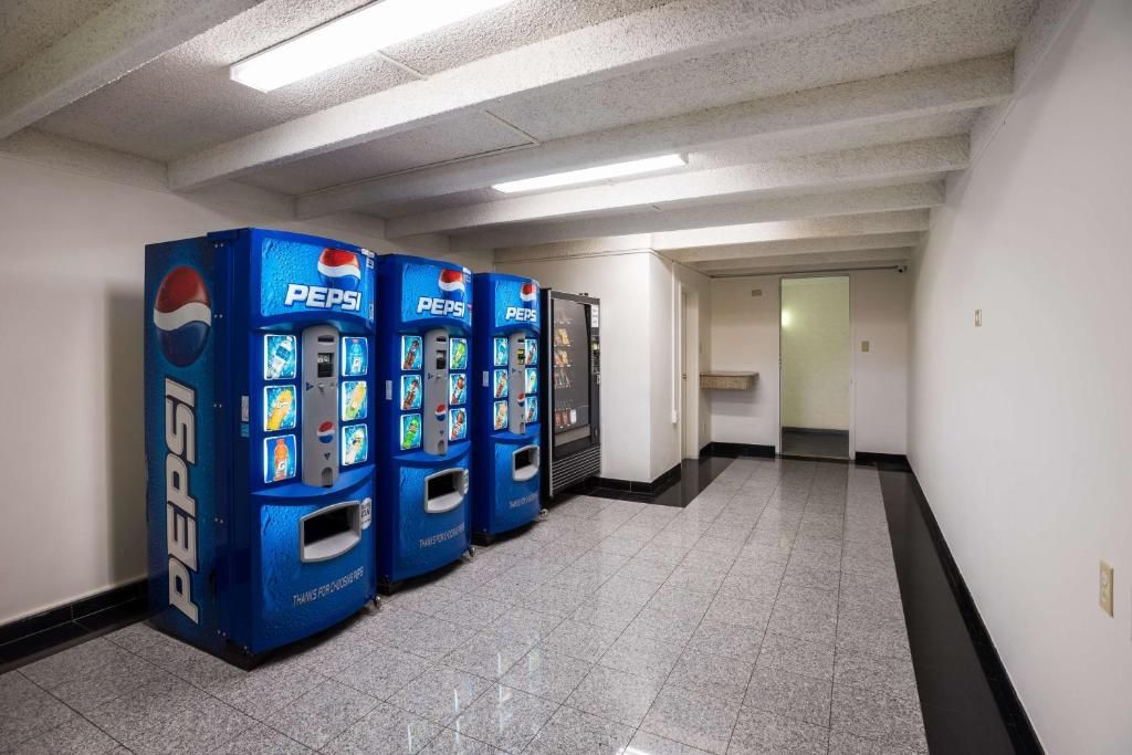 Un couloir où sont alignés contre le mur trois distributeurs automatiques de Pepsi, tous bleus.
