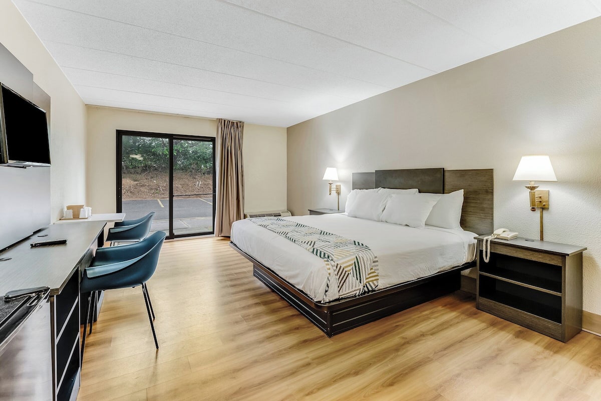 A hotel room with a bed, bedside tables, a desk, and chairs.