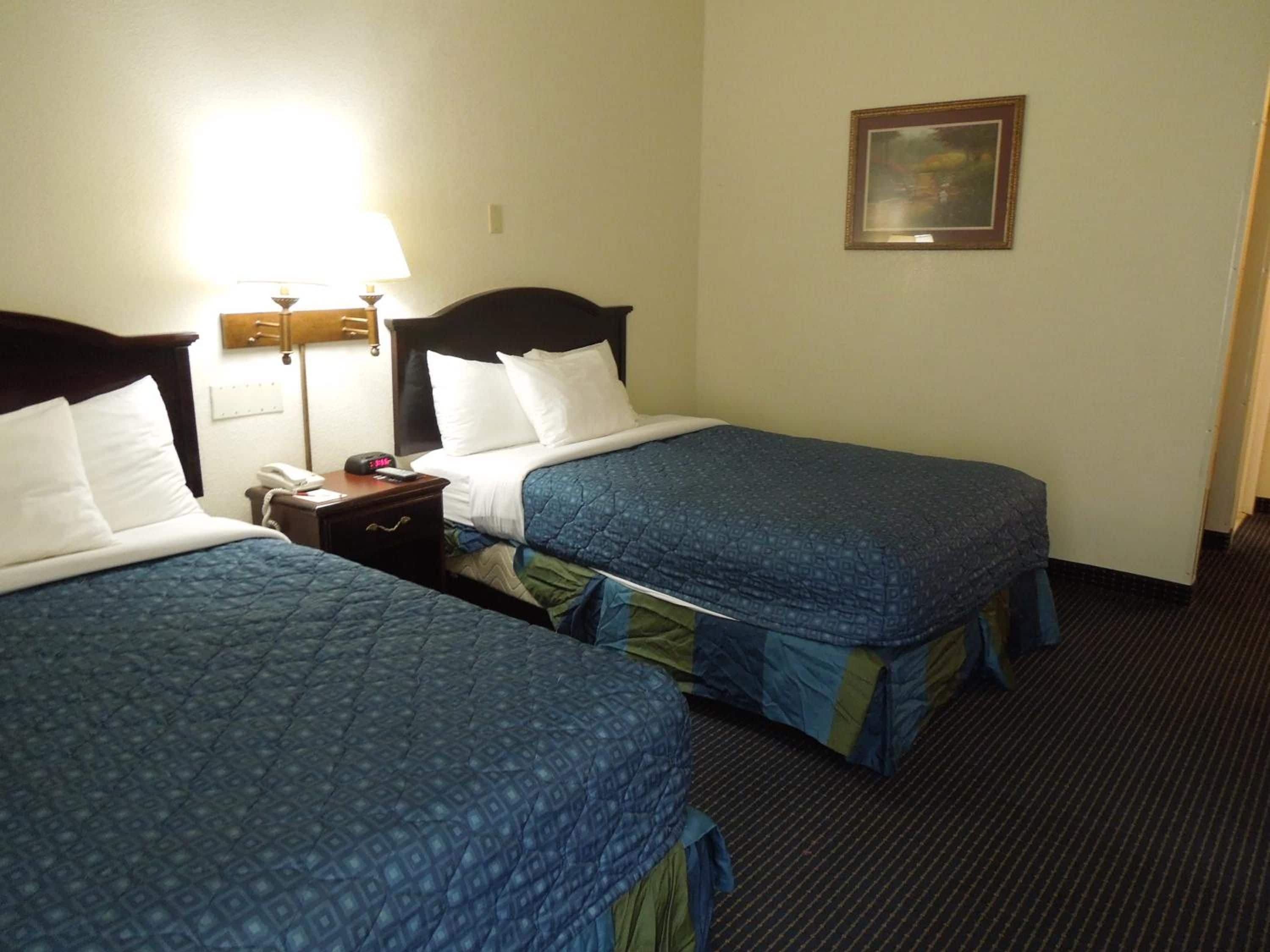 A hotel room with two beds, a nightstand with a lamp, and a framed picture on the wall.