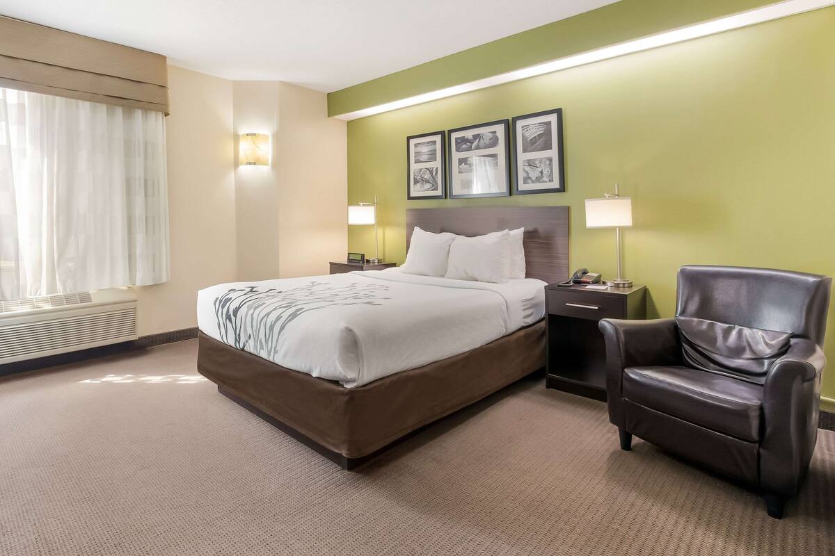 Una habitación de hotel con una cama grande, una silla, una mesita de noche y lámparas fijadas a la pared.