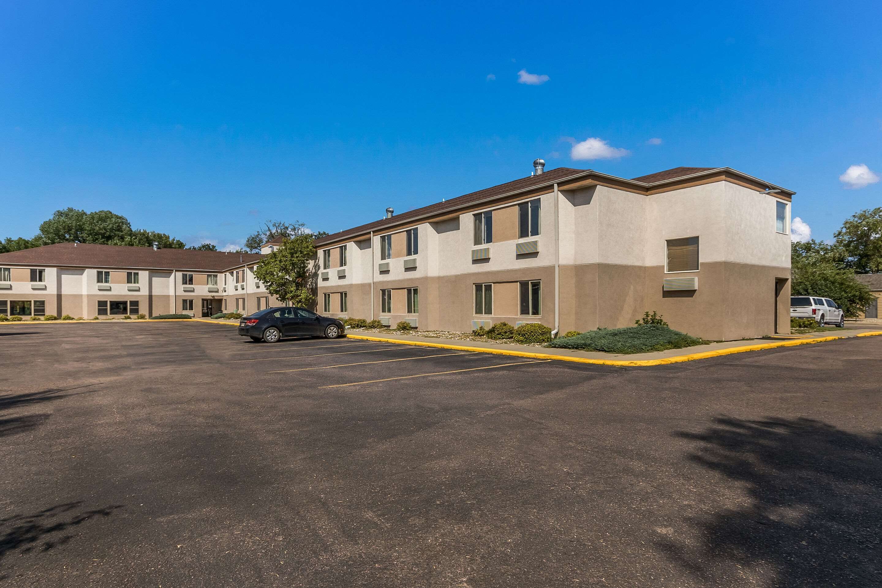 A multi-story hotel with a parking lot, a black car parked in the lot, and a clear blue sky.