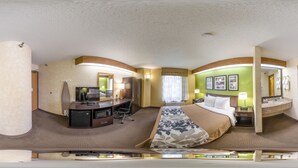 Habitación de hotel con distribución curva, una cama, un escritorio, una silla, un televisor, una mesita de noche, una lámpara y un baño con inodoro y lavamanos.