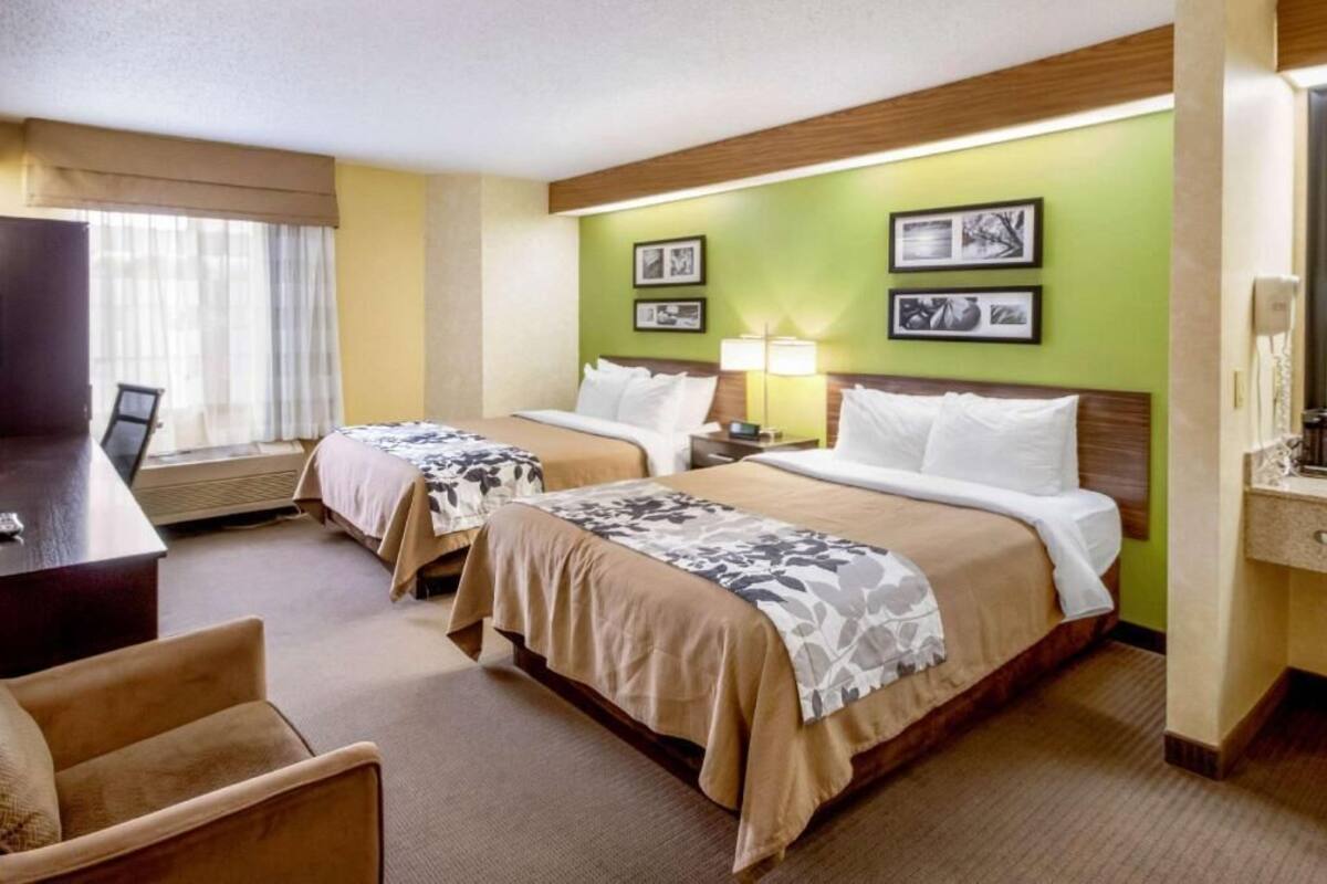 Una habitación de hotel con dos camas, un escritorio, una silla y una ventana con cortinas.