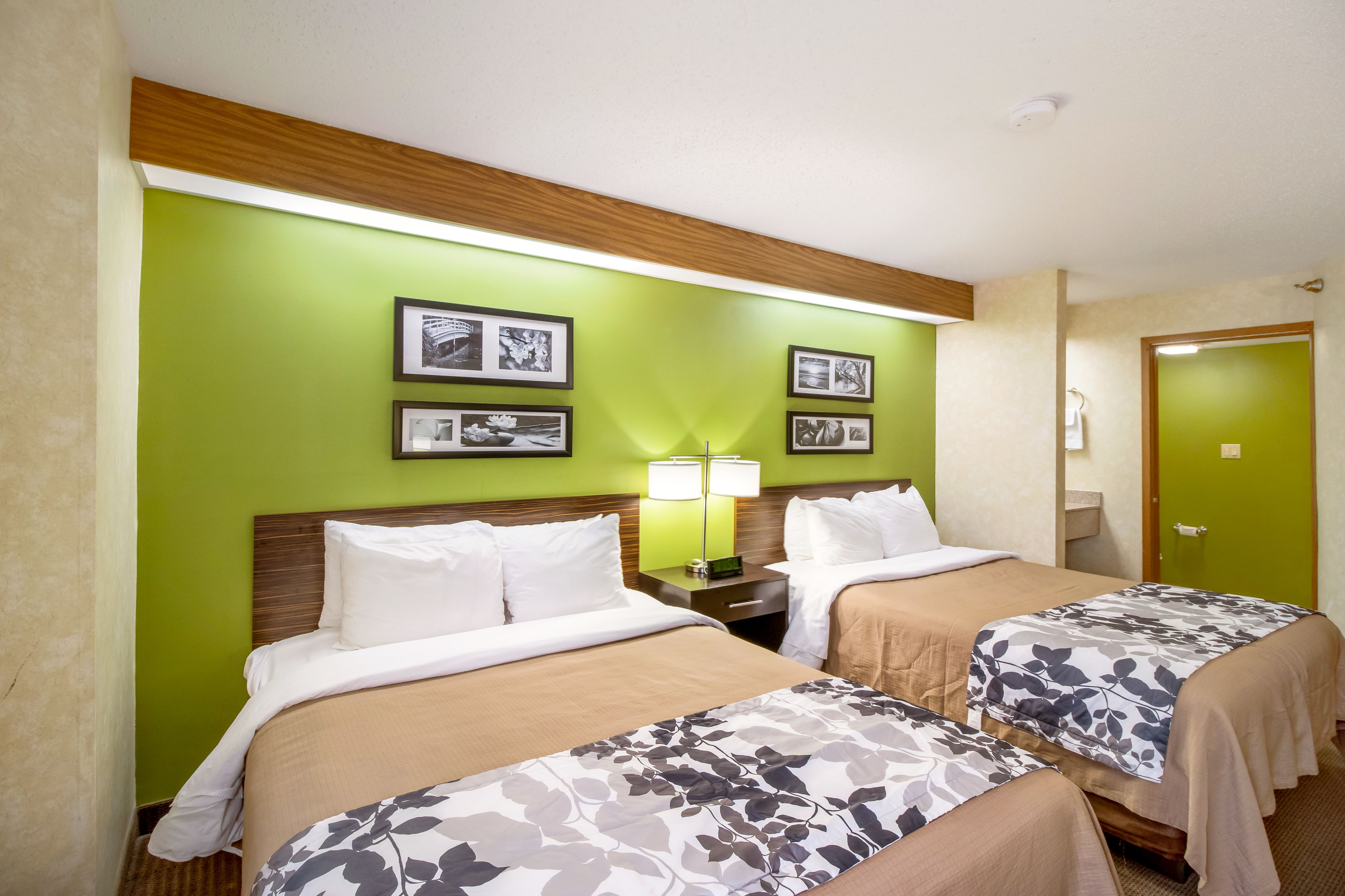 A hotel room with two beds, green walls, framed pictures, and a wooden headboard.