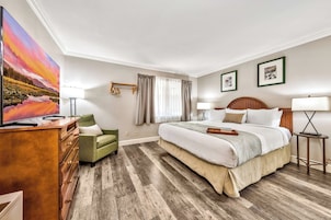 A hotel room with a bed, a dresser, a chair, a television, and a window with curtains.