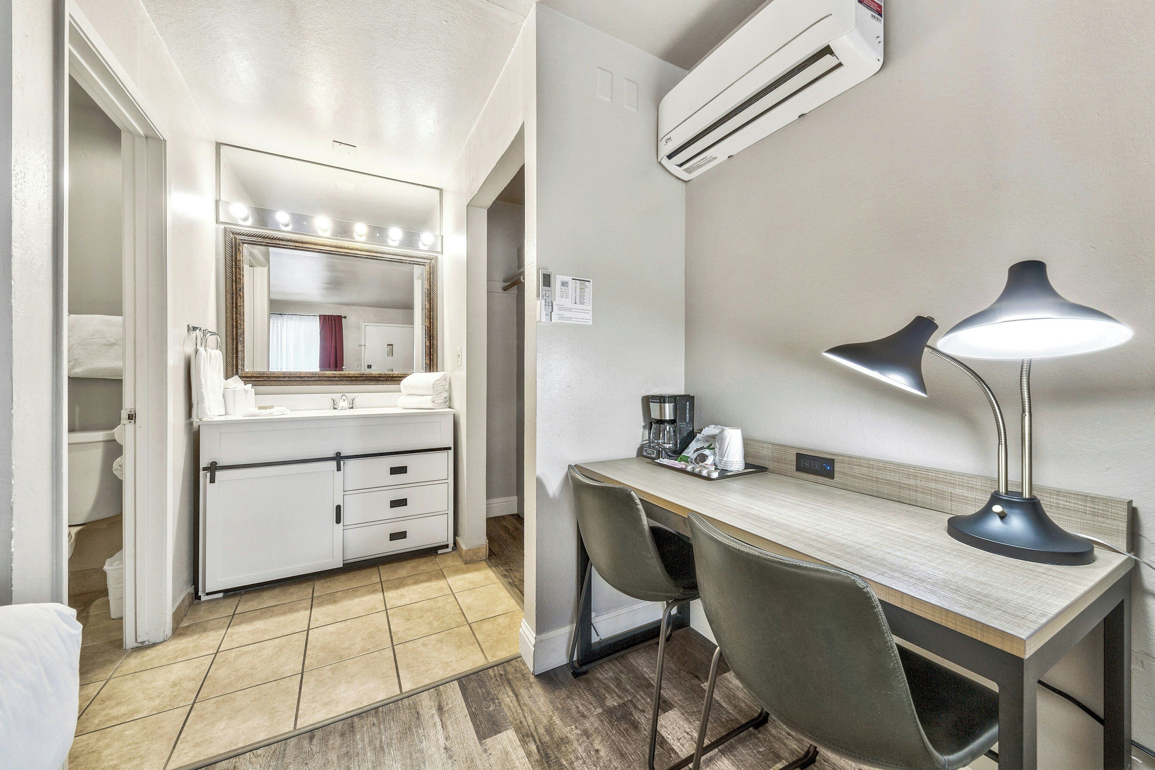 Een hotelkamer met een badkamer, een bureau met twee stoelen, een bureaulamp en een airconditioning.