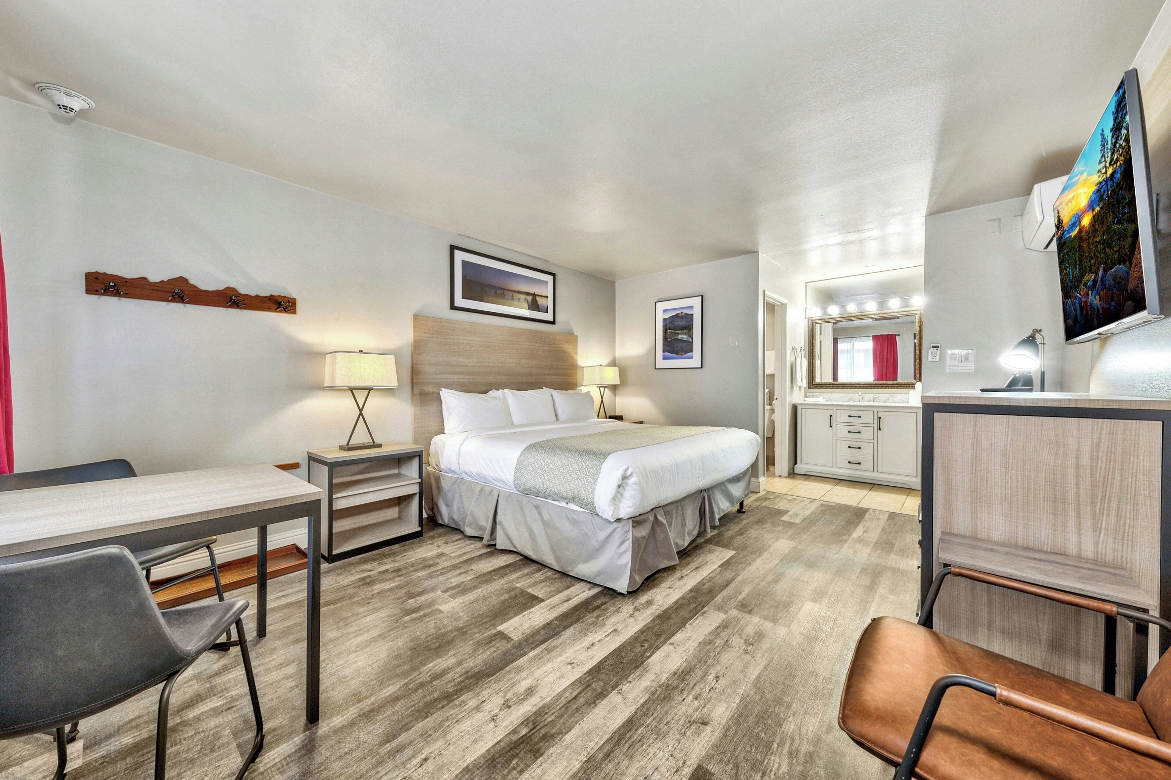 A hotel room with a bed, bedside tables, a desk, a chair, a mirror, and artwork on the walls.
