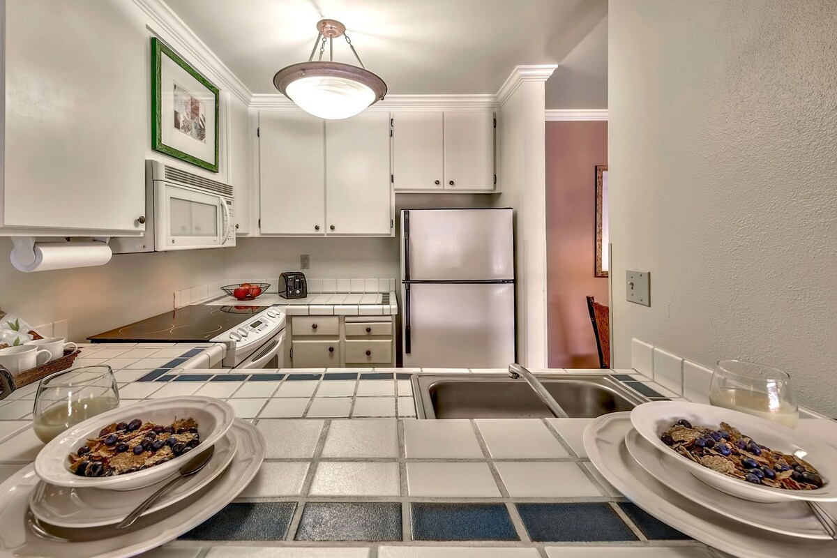Una cocina moderna con armarios blancos, un refrigerador de acero inoxidable, una estufa a gas y un salpicadero de azulejos.