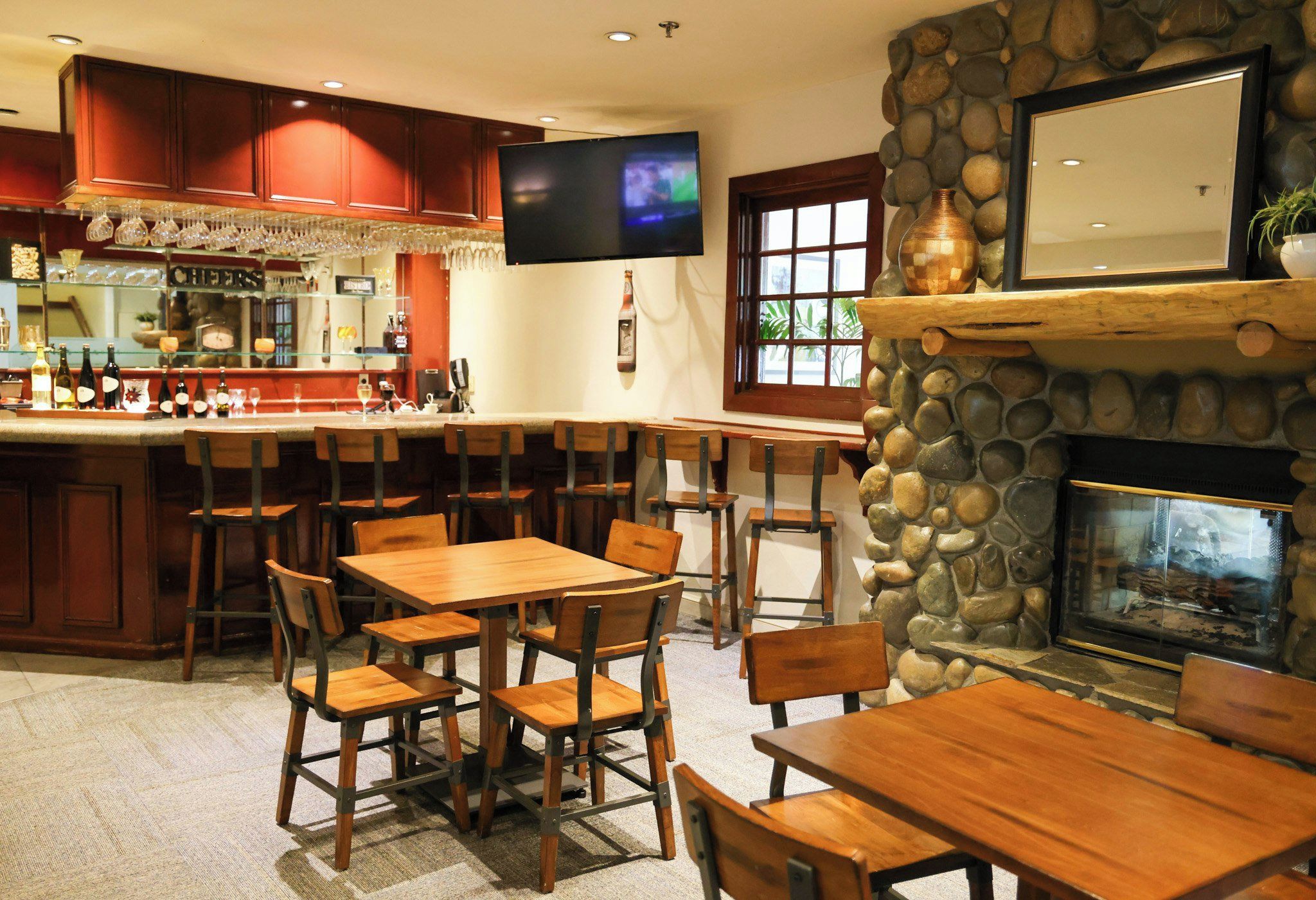 A bar area with wooden furniture, a television mounted on the wall, and a stone fireplace.