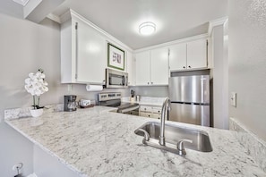 A kitchen with white cabinets, a stainless steel refrigerator, a microwave, a stove, and a sink with a modern faucet.