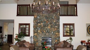 A spacious living area with a high wooden ceiling, a stone wall, and two leather sofas.