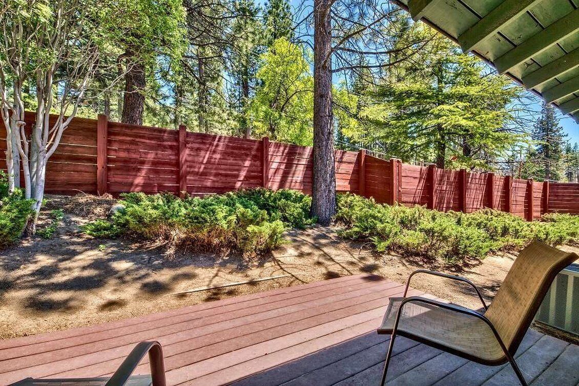 A wooden deck with a chair, surrounded by a red fence and trees.