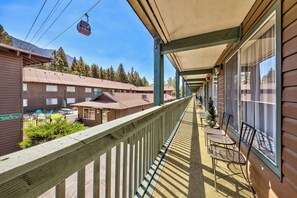 Un balcón de hotel con mobiliario exterior, vistas de los alrededores y un teleférico al fondo.