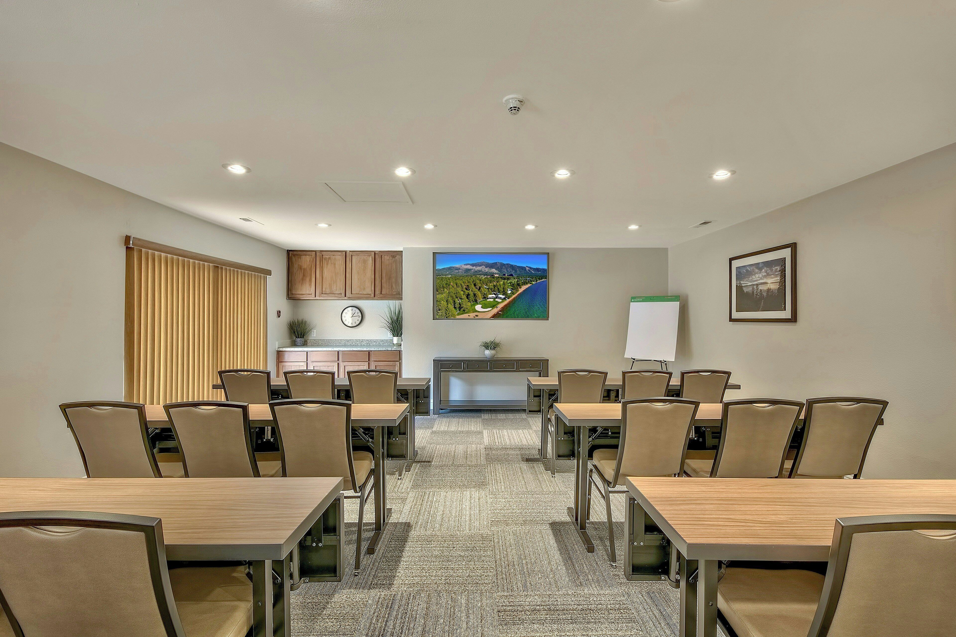 A conference room with a large table, chairs, a clock, a plant, and a painting of a landscape.