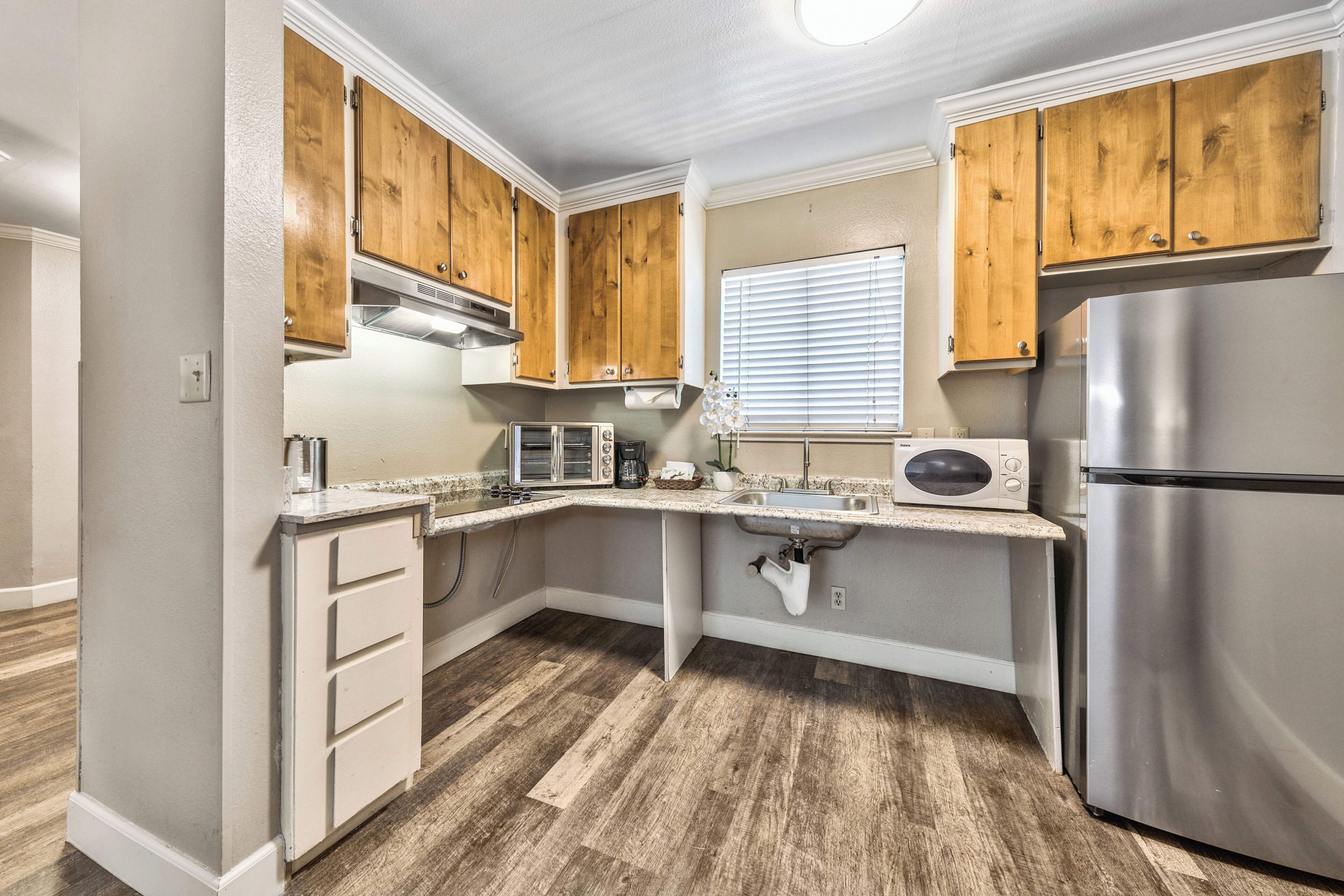 A compact kitchen with wooden cabinets, a stainless steel refrigerator, a microwave, and a built-in oven.
