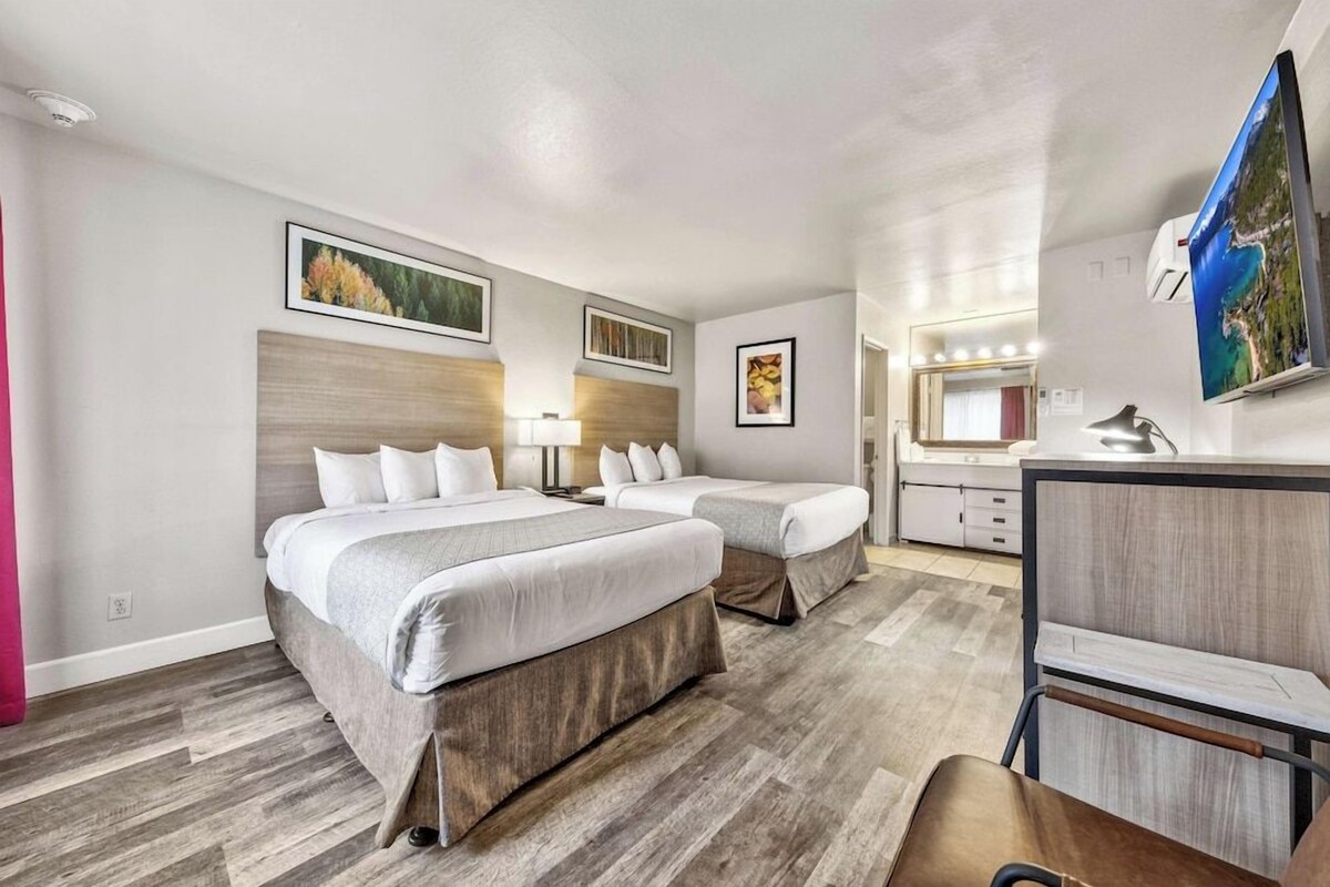 Habitación de hotel con dos camas, un escritorio, una silla, un televisor y obras de arte en las paredes.