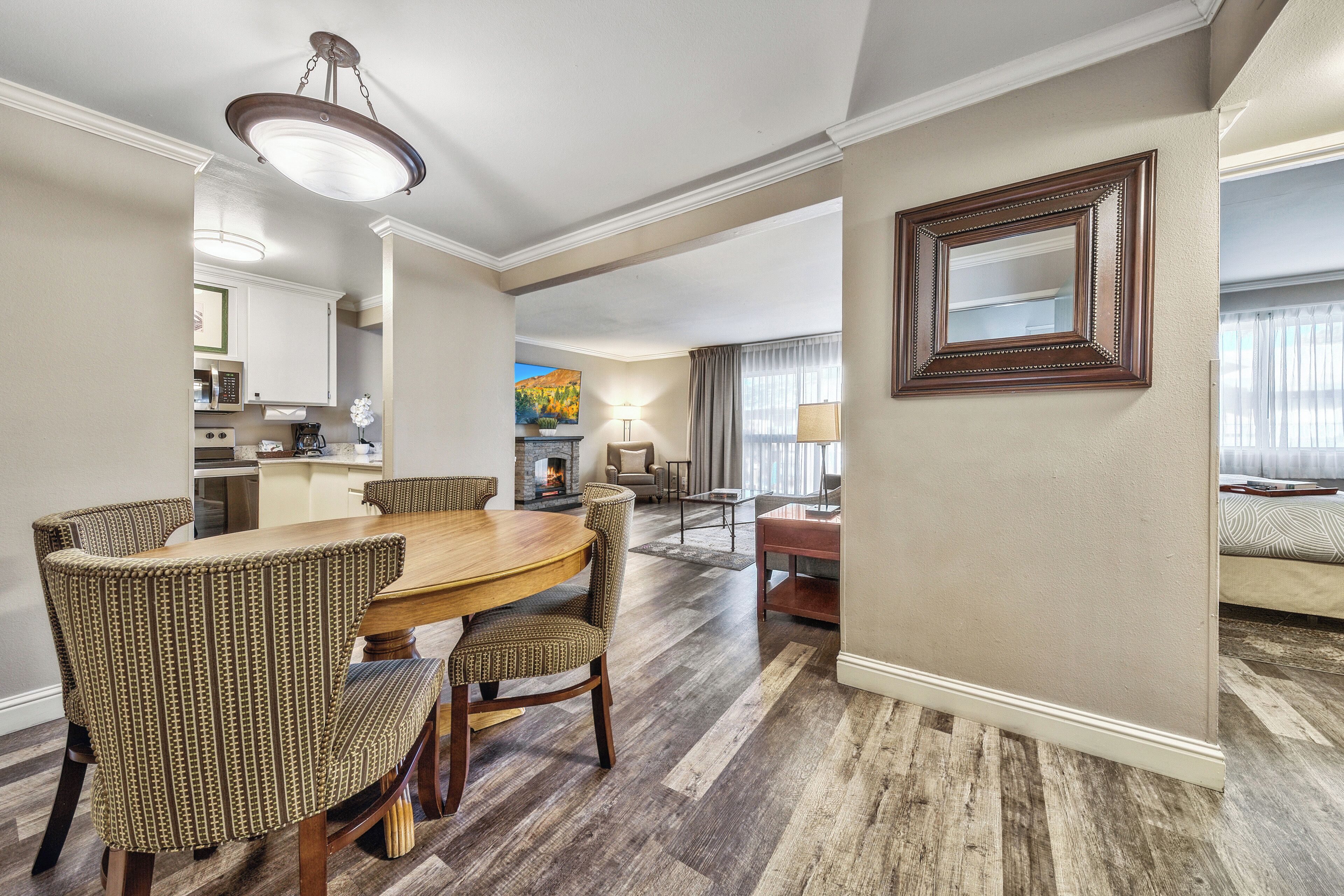 A spacious dining area with a wooden table and patterned chairs, a kitchen in the background, and a living area with a fireplace.