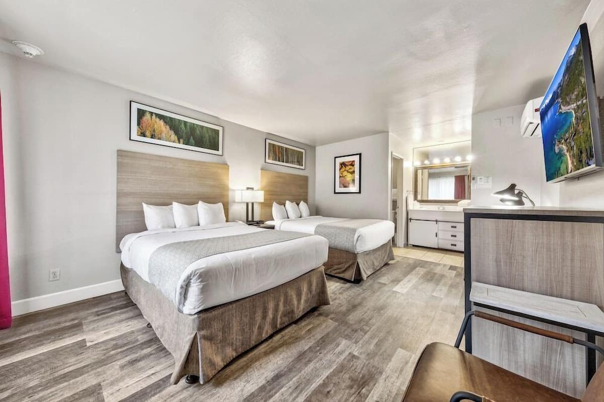 Une chambre d’hôtel avec deux lits, un bureau, une chaise, une télévision et une salle de bain équipée d’un miroir et d’un lavabo.