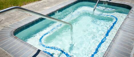 A rectangular hot tub with a tiled edge and a metal ladder.