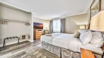 A hotel room with a bed, a dresser, a chair, a desk, a lamp, and a painting on the wall.