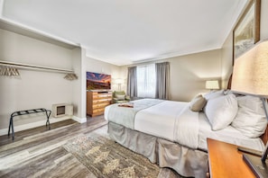 A hotel room with a bed, a dresser, a chair, a desk, a lamp, and a painting on the wall.