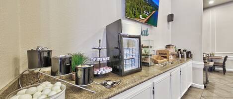 A kitchen area with a granite countertop, a coffee machine, a refrigerator, and a bowl of eggs.