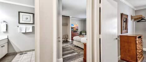 A hallway with a bathroom on the left, a bedroom with a bed and dresser in the center, and a closet with a wooden dresser on the right.