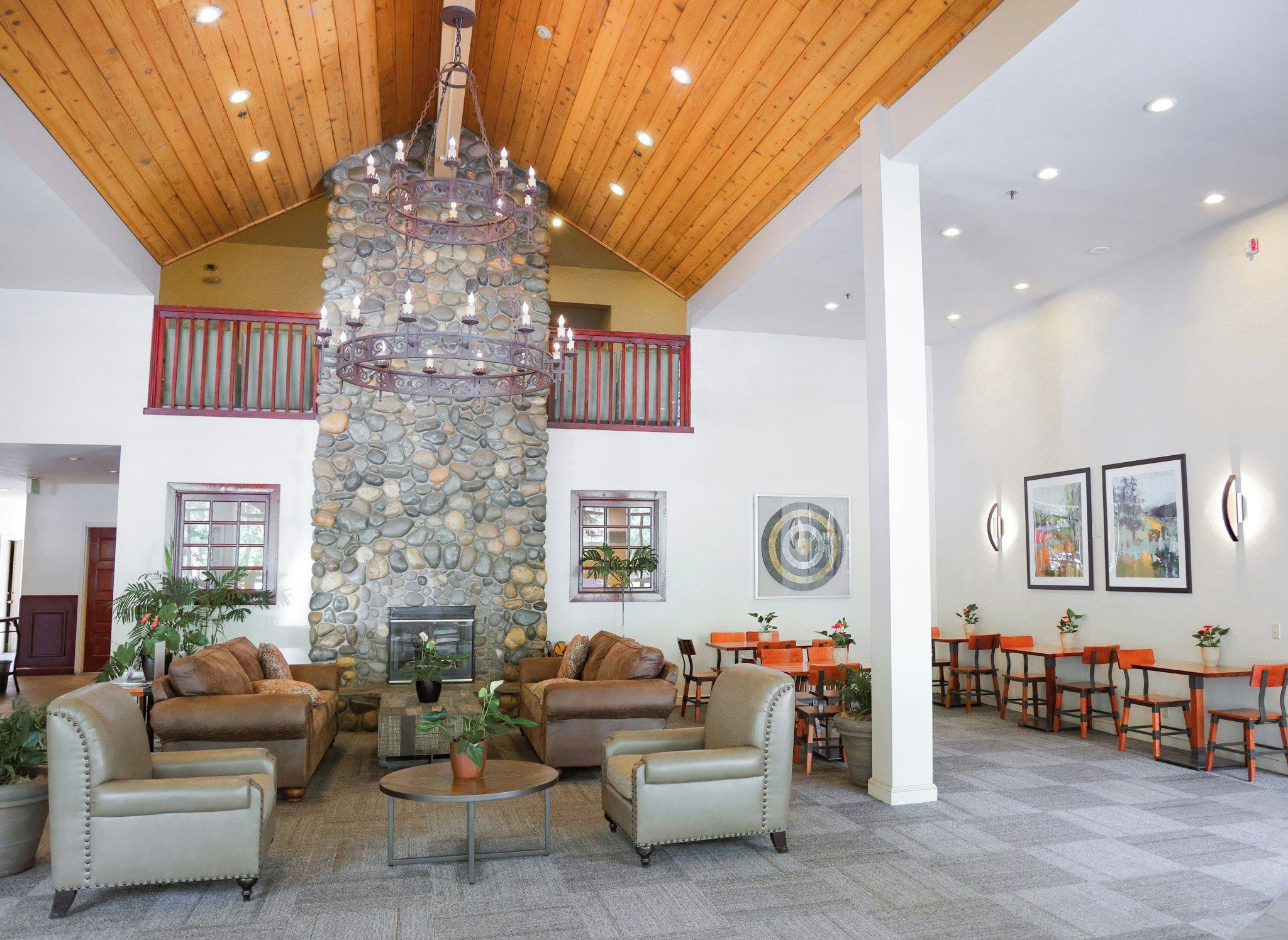 A spacious lobby with a stone fireplace, leather sofas, and a dining area with orange chairs.