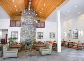 A spacious lobby with a stone fireplace, leather sofas, and a dining area with orange chairs.