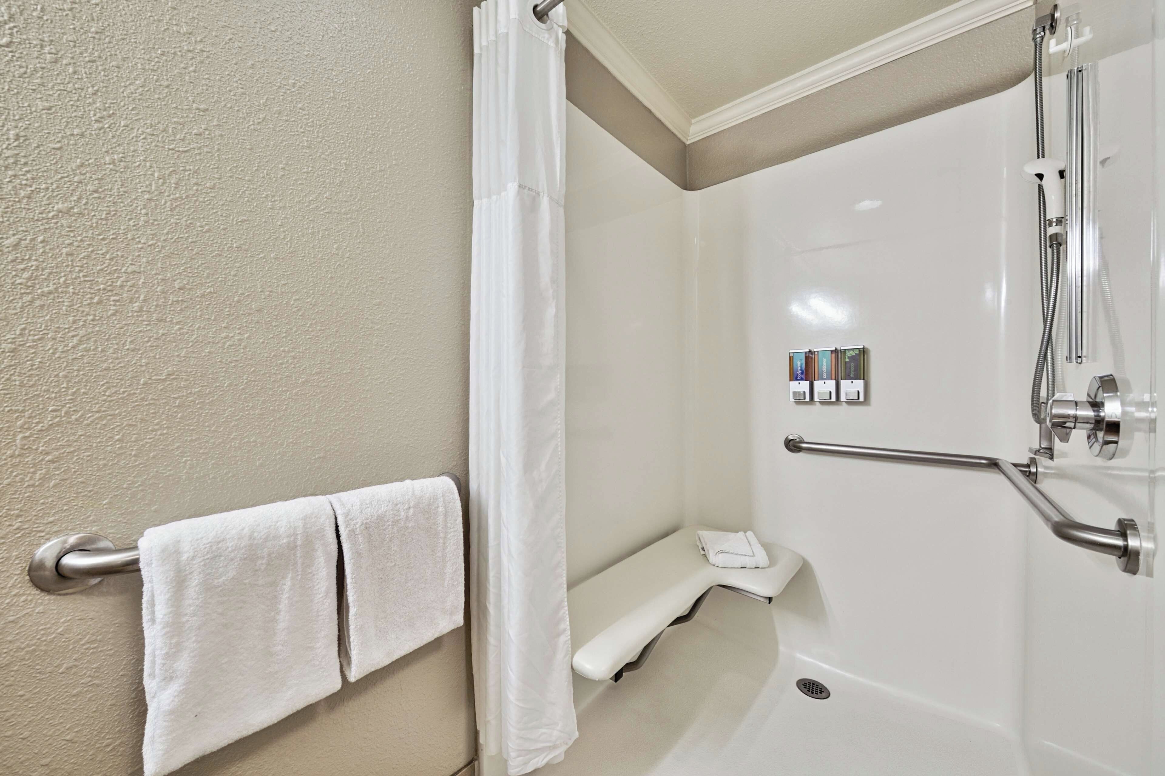 A bathroom with a shower, a towel rack with two towels, a grab bar, and a set of toiletries.