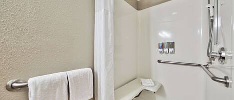 A bathroom with a shower, a towel rack with two towels, a grab bar, and a set of toiletries.