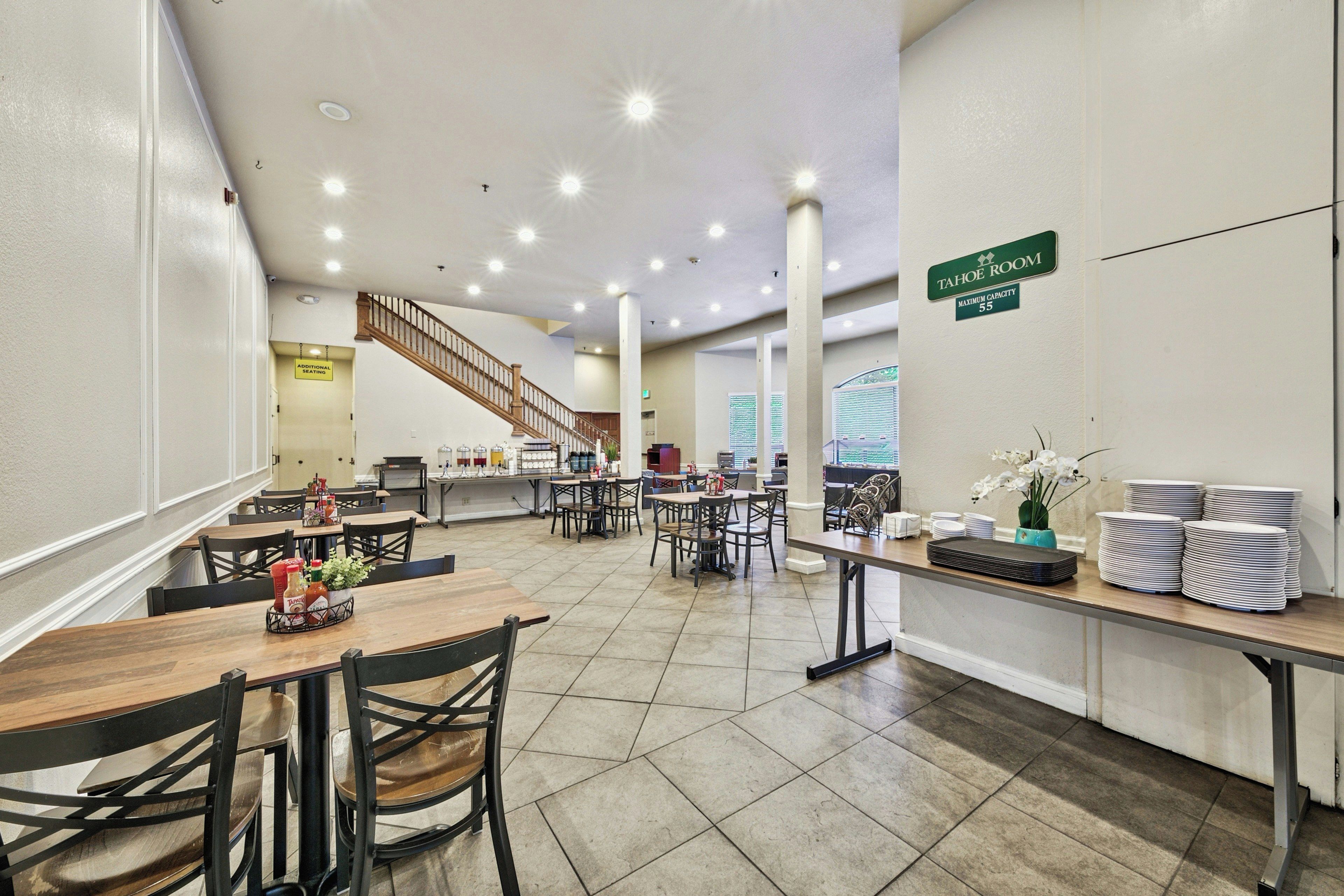 A hotel dining area with multiple tables and chairs, a staircase, and a sign indicating a room with a maximum capacity of 55.