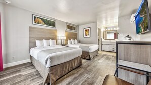 A hotel room with two beds, a desk, a chair, and a TV.