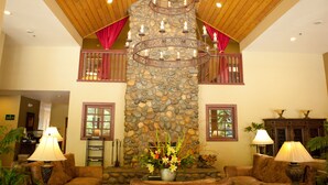 A lobby with a stone pillar, wooden ceiling, and red curtains. There are two lamps on either side of a central floral arrangement.