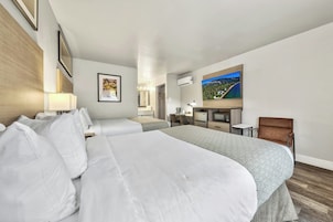 Habitación de hotel con dos camas, un escritorio, una silla, un televisor y baño con espejo y lavamanos.