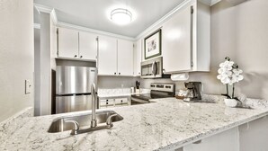 A kitchen with white cabinets, stainless steel appliances, a marble countertop, and a potted orchid.