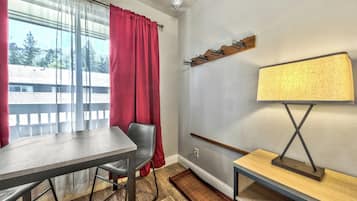 A room with a dining table, a chair, a lamp, and a coat rack.
