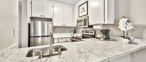 A kitchen with white cabinets, a stainless steel refrigerator, a built-in oven, and a coffee maker.