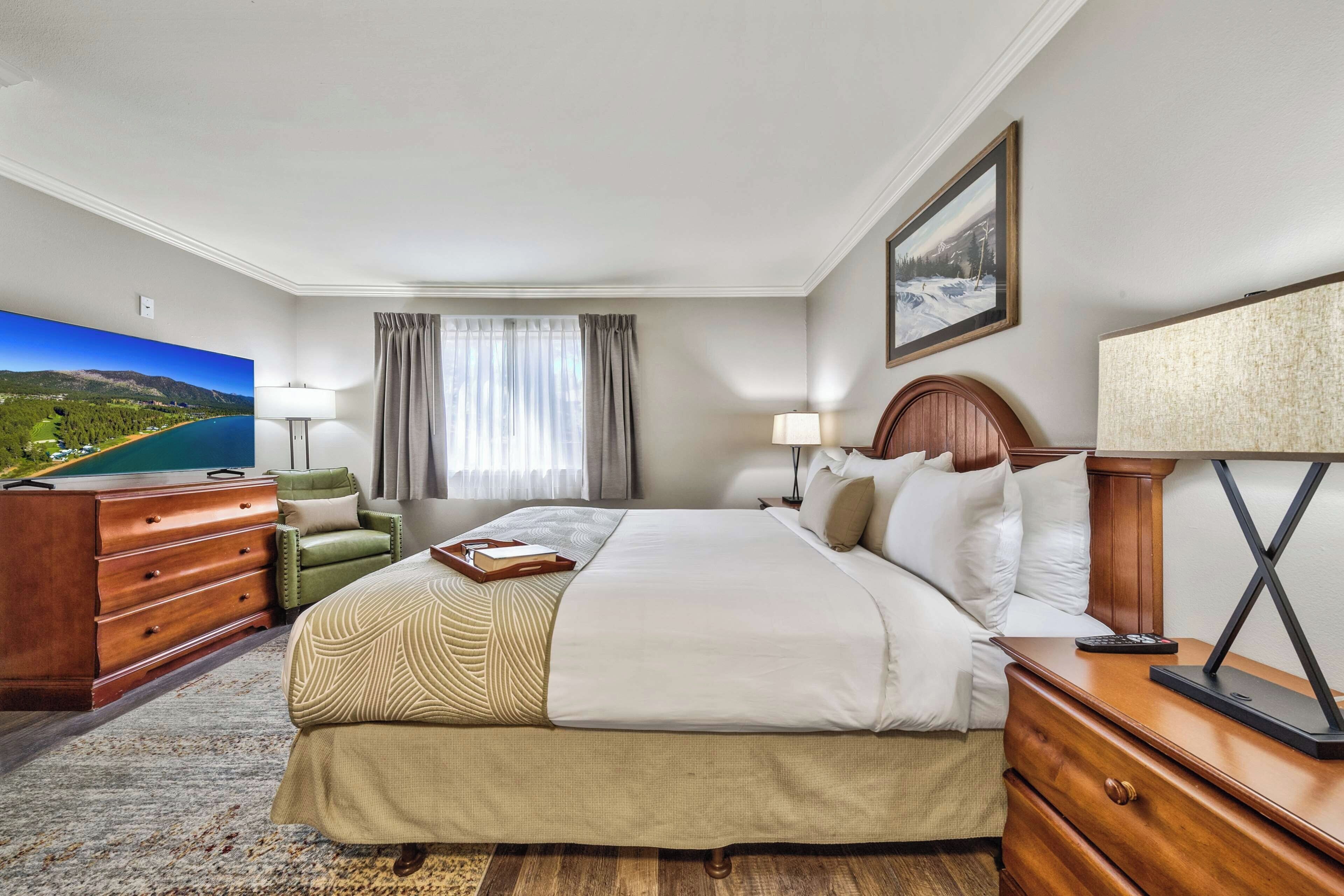 A hotel room with a bed, a desk, a chair, a television, and a painting on the wall.