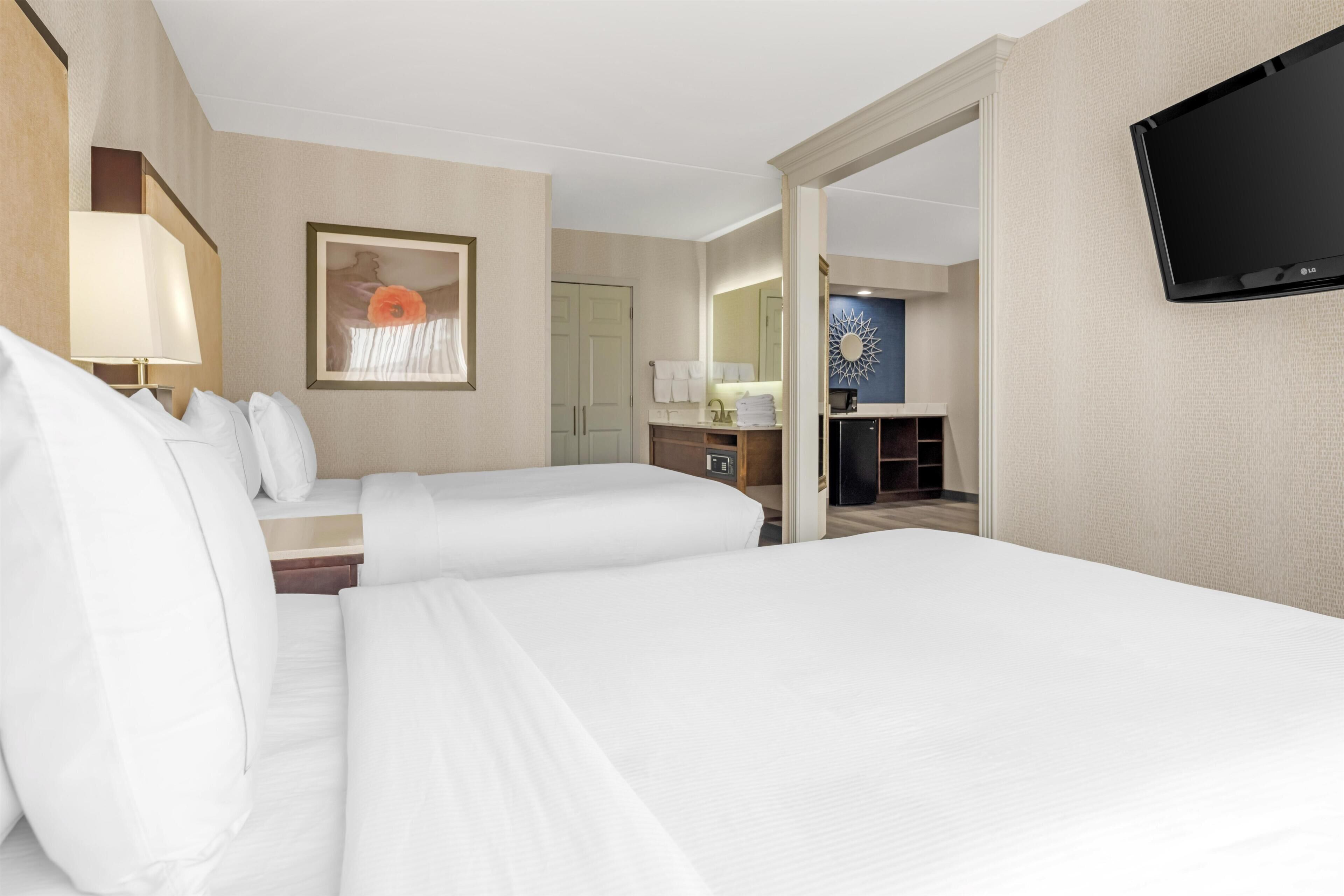 Ein Hotelzimmer mit zwei Betten, einem Fernseher, einem Gemälde, einem Schreibtisch und einem Badezimmer.