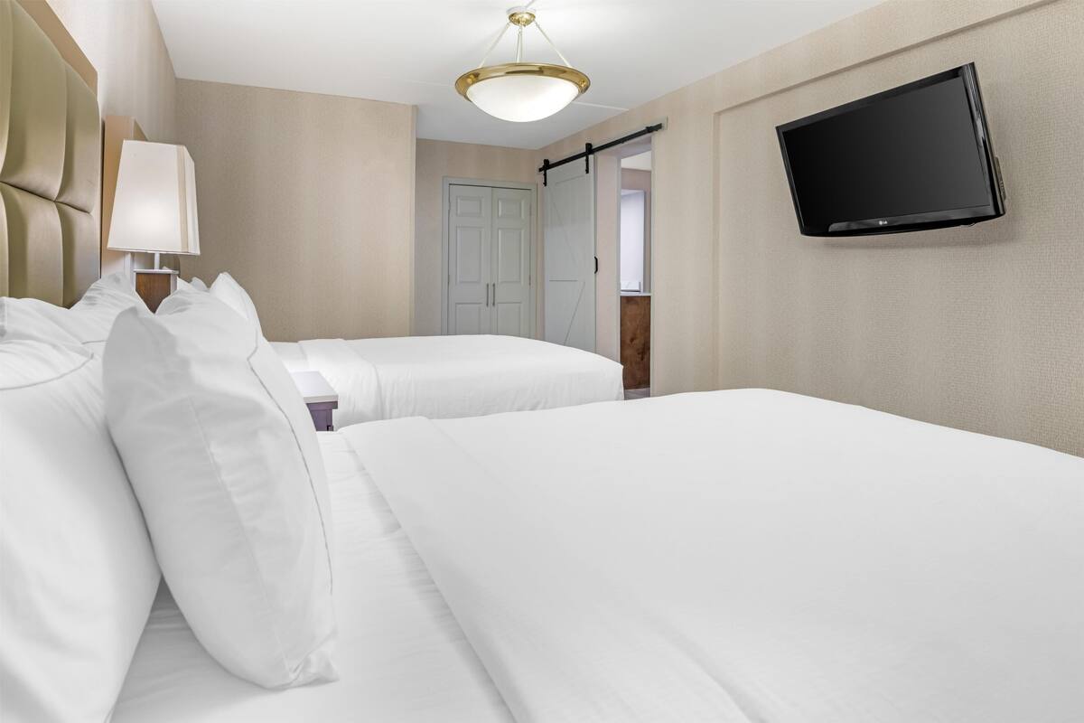 Ein Hotelzimmer mit zwei Betten, einem Fernseher, einer Lampe und einer Tür zu einem Badezimmer.