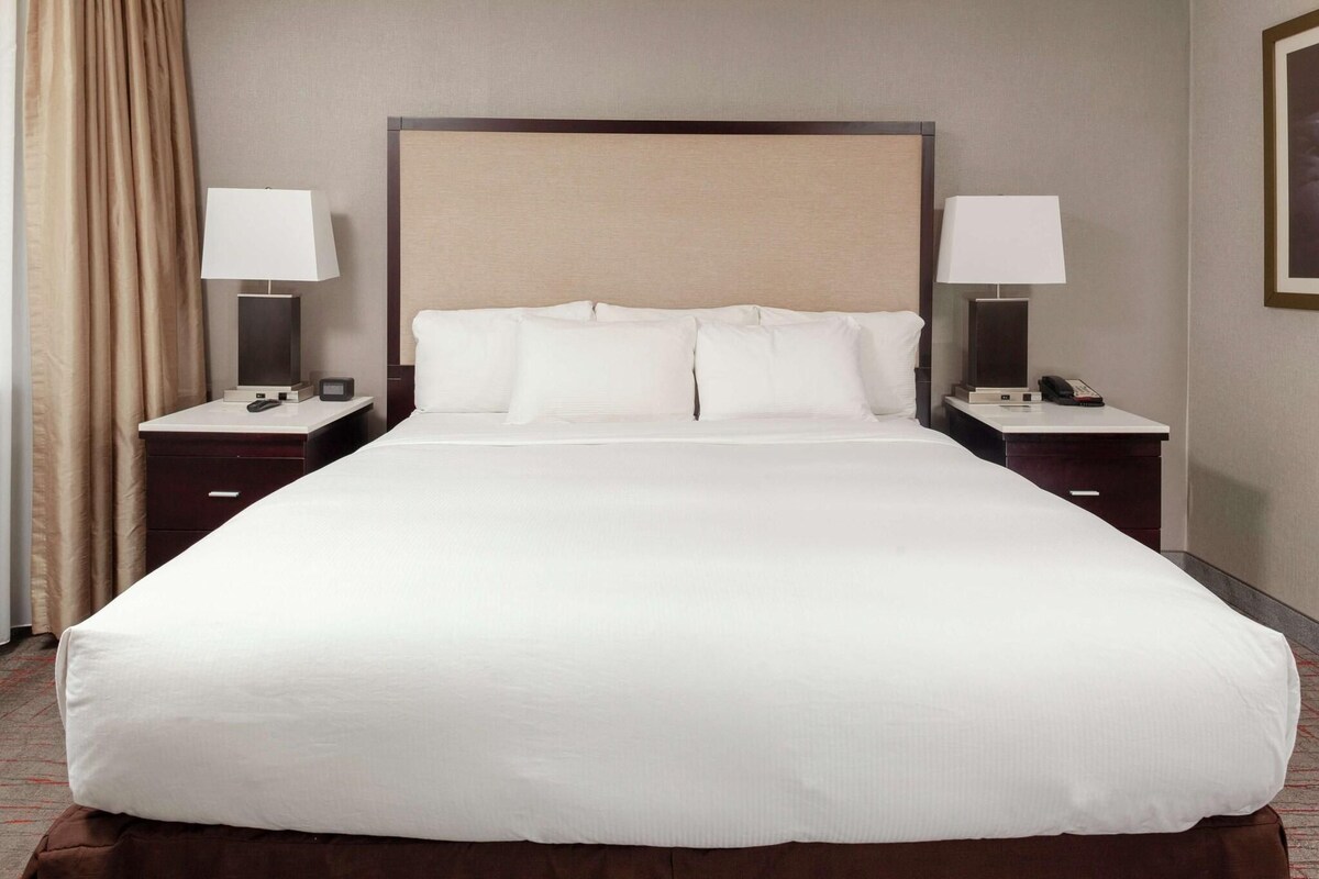 Una cama grande con sábanas blancas, dos mesitas de noche con lámparas y un cabecero.