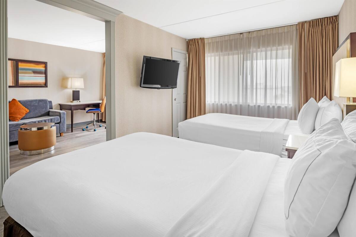Ein Hotelzimmer mit zwei Betten, einem Fernseher, einem Schreibtisch mit Stuhl und einem Sofa.