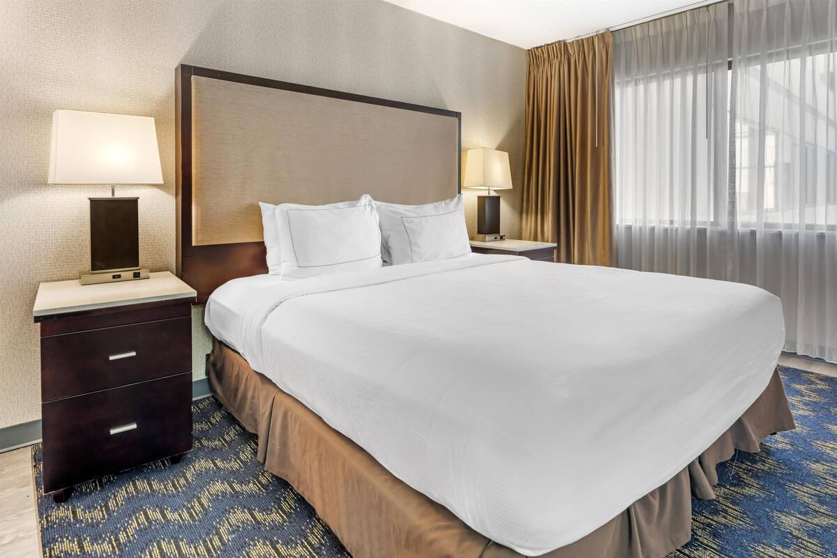 Ein Hotelzimmer mit einem großen Bett, zwei Nachttischen, einer Kopfteil und einem Vorhangfenster.
