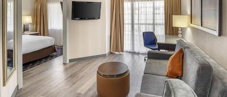 Une chambre d’hôtel avec un lit, un canapé, une table basse ronde, une télévision et une fenêtre avec des rideaux.