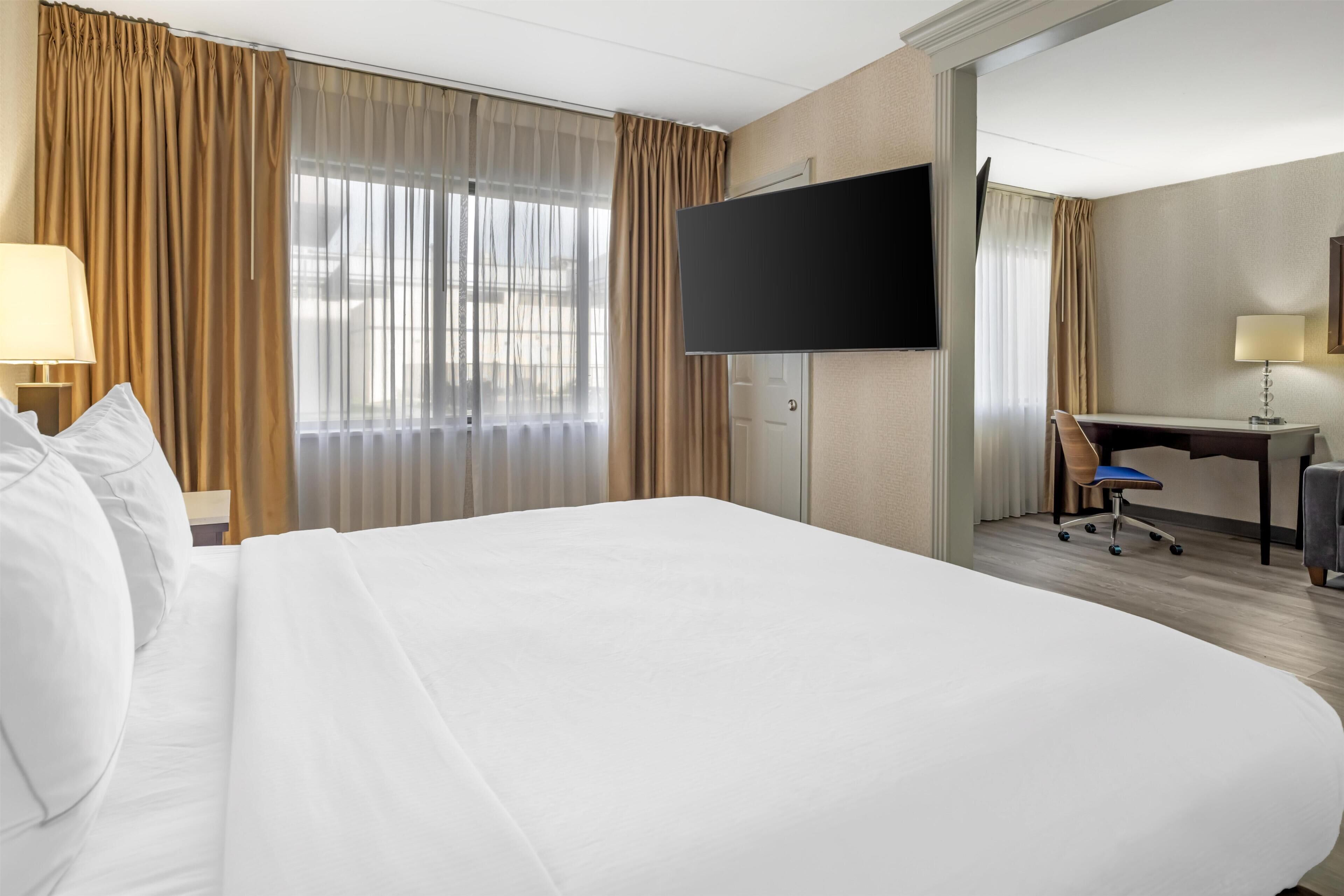 Une chambre d’hôtel avec un grand lit, un bureau, une chaise, une télévision et des rideaux.